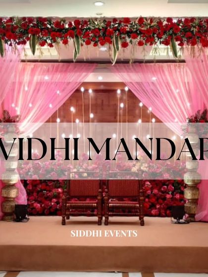 A Vidhi Mandap that radiates passion and romance. The stage is enveloped in soft pink curtains and decorated with an abundance of rich red flowers, creating a dramatic and opulent setting.
