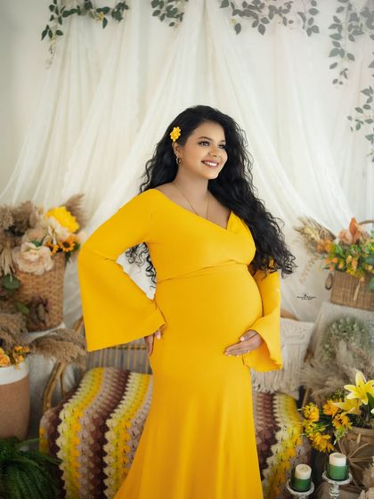 A radiant portrait of a mother-to-be. Her joyful expression and the vibrant yellow of her gown and the set create an image full of life and happiness.