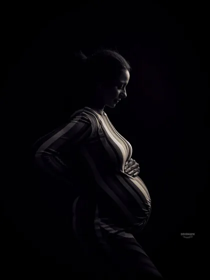 A contemplative and artistic silhouette. The client is looking down, cradling her bump, and the rim lighting beautifully traces her shape, creating a quiet and emotional black and white portrait.