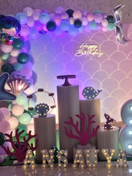 A magical mermaid party setup with an iridescent scale backdrop, a neon sign, and light-up sea-themed props.