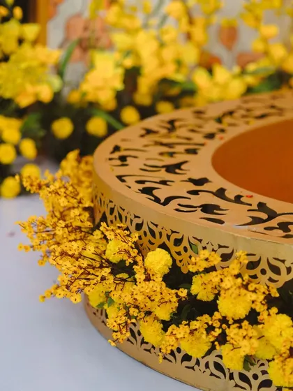 A close-up of the intricate details in our decor. This laser-cut golden container filled with vibrant yellow flowers was part of a colorful Haldi ceremony setup.