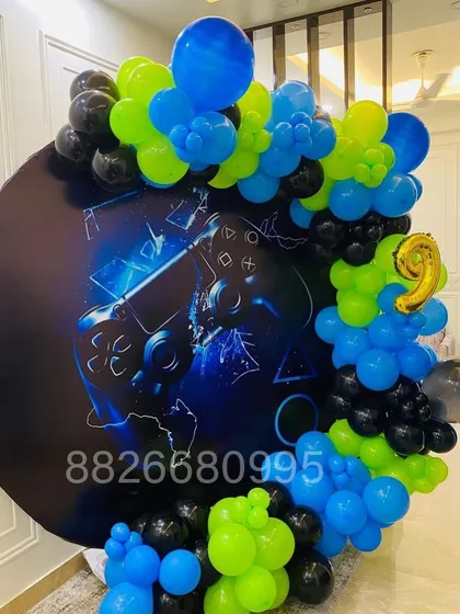 I can create decorations for any theme, including this popular gaming party setup for a 9th birthday. It features a custom printed backdrop with a game controller graphic, framed by a balloon garland in matching blue, green, and black.