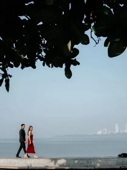 A beautifully framed shot of the couple walking along Mumbai's Marine Drive, with the city skyline in the distance, creating a sense of urban romance.