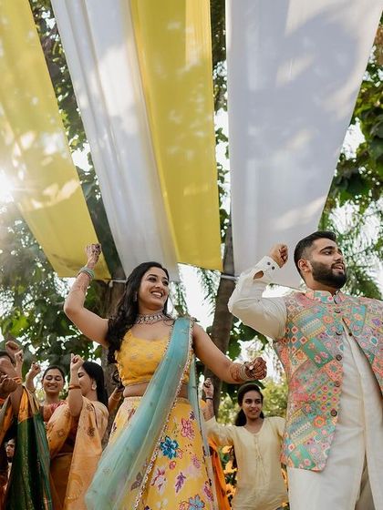 Dancing their way into the Haldi celebration under drapes of yellow and white fabric, the couple is full of energy and excitement.