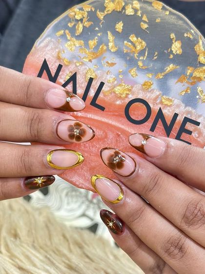 A closer look at the brown floral nail art, showing the precise details of the petals and the sparkle of the central rhinestone. Each element is carefully placed to create a balanced and beautiful composition.