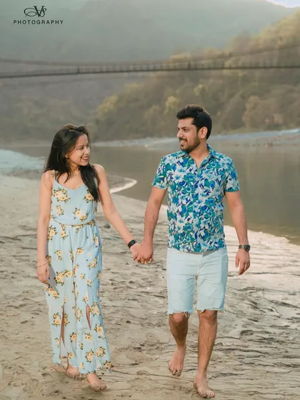 A candid shot of a couple walking hand-in-hand along the banks of the Ganges in Rishikesh. The natural setting and the iconic Laxman Jhula bridge in the background make this a memorable destination photo.