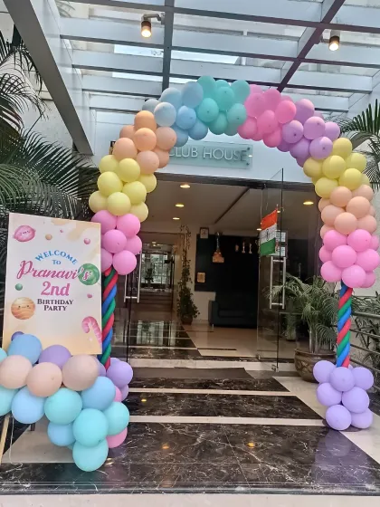 A beautiful pastel rainbow balloon arch at the entrance to a clubhouse for a 2nd birthday party. It's a cheerful and inviting way to greet guests.