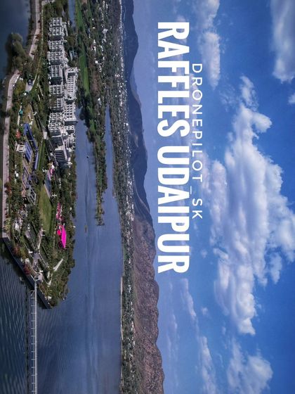 A high-altitude photograph of Raffles Udaipur, showing the private island location and the sprawling estate. This static image gives a clear sense of the property's scale and its stunning position within the lake.