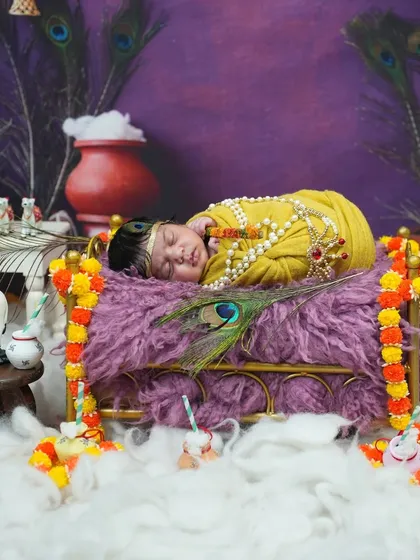 This newborn Krishna setup features a miniature cot decorated with marigold flowers, a tiny cow figurine, and a pot of butter, telling a complete story.