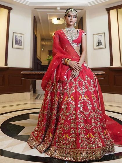 A full-length view of a stunning red lehenga. The makeup is glamorous and bold, with a focus on the eyes, creating a look that is perfect for an evening ceremony.