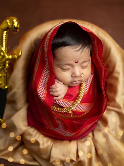 A gentle and serene portrait, with the baby's head turned slightly, showcasing the traditional wrap and the golden sword hilt.