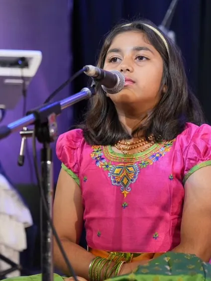 A young student sings a devotional song at Kalaa Sangama 2024. She is dressed in traditional attire for her performance of Purandara Dasa Keertane.