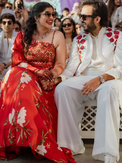 A seated portrait of the couple at their welcome event. This shot gives a great view of the bride's one-shoulder blouse and the groom's rose-embroidered jacket, a perfectly coordinated look.