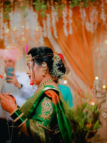 A side profile of the bride during the antarpat ritual. The focus is on her traditional attire, intricate hairstyle with flowers, and the sacred thread in her hands.