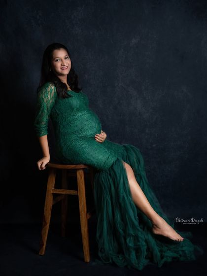 An elegant pose in an emerald green lace gown. The dark, moody backdrop helps to highlight the rich color of the dress and the beautiful silhouette of the mother-to-be.