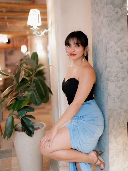 A stylish indoor portrait. The model's pose against the wall and the soft ambient light create a chic and relaxed lifestyle shot.