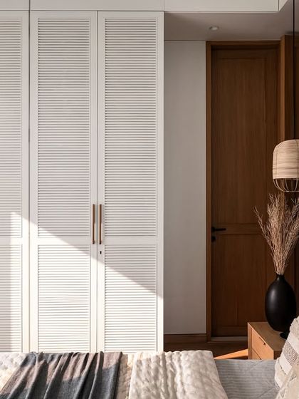 White matt PU-finished louvred wardrobes discreetly provide ample storage in this master bedroom. This design choice helps maintain an uncluttered and airy ambiance in the room.