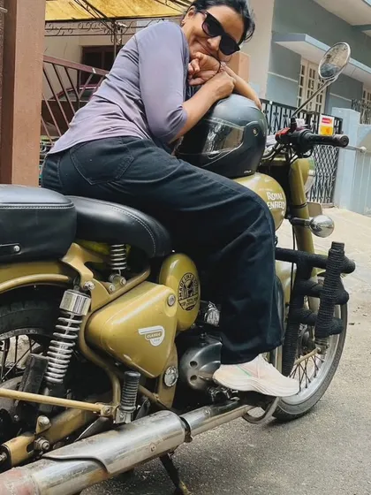 A graduate takes a well-deserved rest, leaning on her helmet. She has earned her place on the road and is a true Royal Enfield rider.