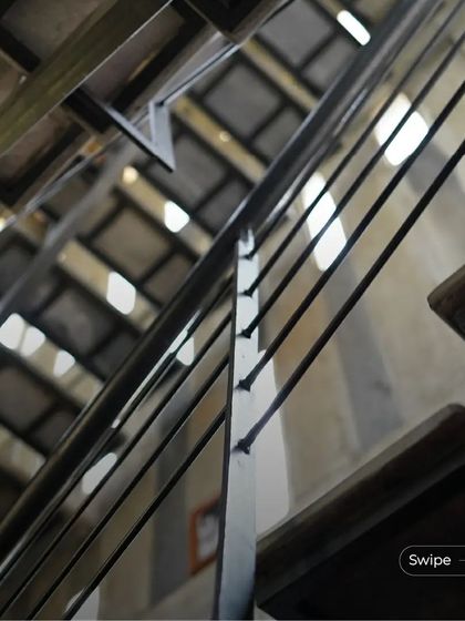 An upward view of the staircase in the Manjunath Residence, showing the interplay of metal railings and the light filtering through the roof tiles.