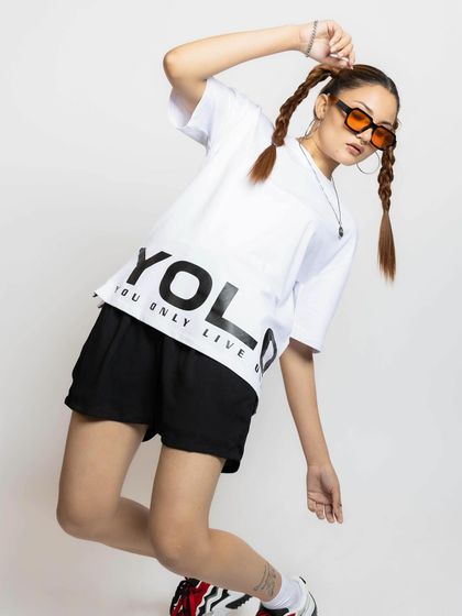 For this look, I styled a white oversized 'YOLO' graphic tee with simple black shorts and chunky sneakers. The pigtails and orange-tinted sunglasses add a playful, retro touch to the outfit.