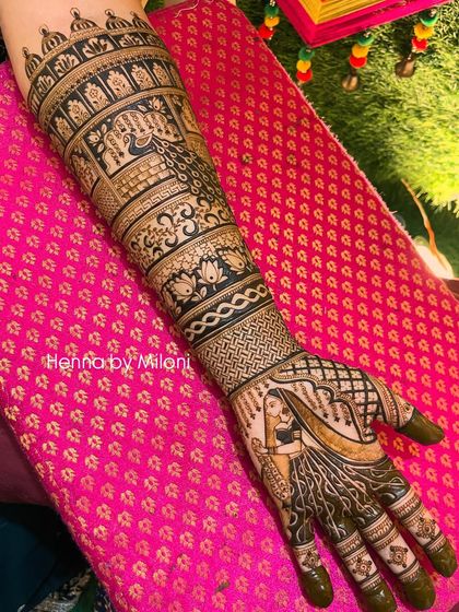 A full-arm bridal mehendi with a beautiful bride portrait on the palm. The design extends all the way up the arm with bands of traditional motifs, including elephants and floral patterns.