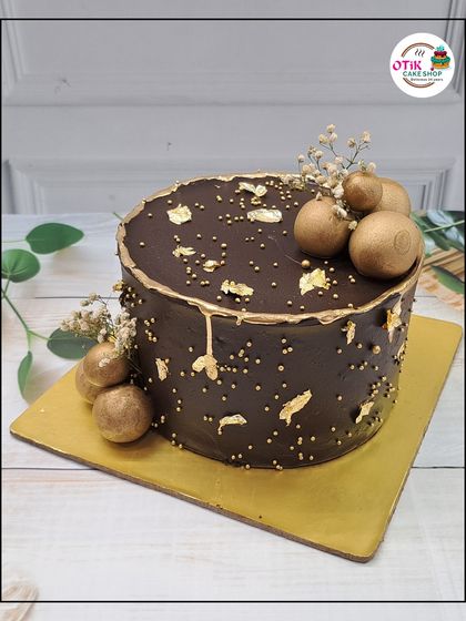A sophisticated take on a chocolate cake. This design features a smooth chocolate ganache, gold leaf flakes, and golden chocolate spheres for a touch of elegance.