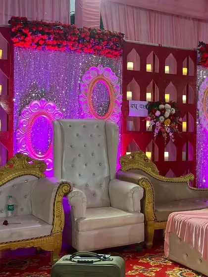 A royal seating arrangement for a wedding, featuring high-back throne chairs and elegant sofas against a red backdrop with a wall of candle-style lights.