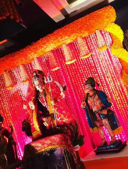 A powerful and traditional setup for a Mata ki Chowki celebration. The decor features a vibrant backdrop of red fabric and stringed flowers, framed by an arch of fresh orange marigolds to create a divine atmosphere.