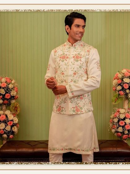 A model smiles in a cream-colored ensemble, where the kurta and jacket are both adorned with matching floral embroidery. This coordinated set is perfect for a daytime festive event.