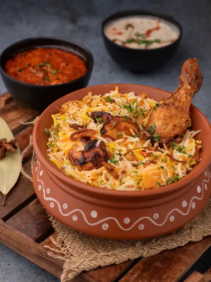 A traditional Chicken Biryani served in an earthen pot. The styling with whole spices and fresh herbs enhances the authentic feel of the dish.
