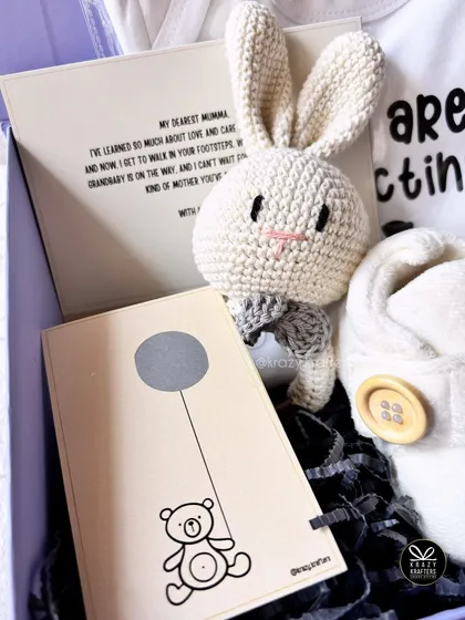 A personalized card for the grandma-to-be, expressing love and excitement, is paired with a cute crochet toy and baby booties.