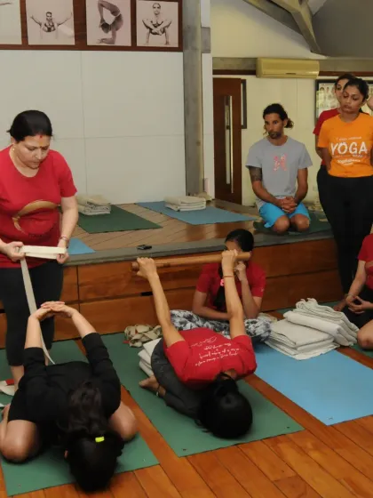 I am demonstrating the use of a belt to help students in a seated forward bend. The belt acts as an extension of the arms, allowing for a deeper and more controlled stretch.