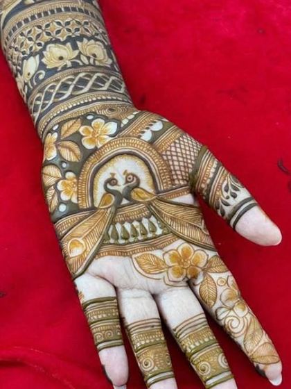 A single hand showing a beautiful design with peacocks and flowers, colored with henna to give it a unique, shaded look.