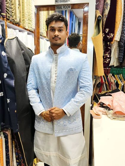 A client wearing a sky blue open Jodhpuri jacket with delicate white embroidery, paired with a white kurta and pant. This is a fresh and contemporary look.