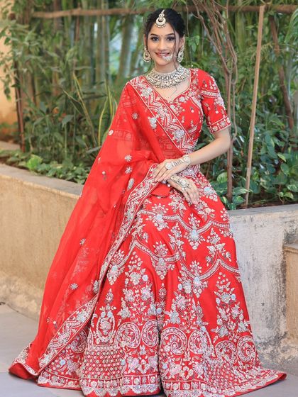 A smiling bride seated in an elegant red lehenga with silver embroidery, paired with a matching diamond and pearl necklace set.