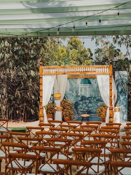 A simple and elegant mandap for a Varapuja function, with a hand-painted backdrop and pots of bright orange marigolds.
