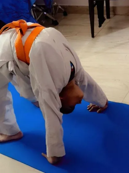 A young student practices a bridge pose, also known as Chakrasana, on a blue mat during a home training session. This demonstrates how our training principles can be applied anywhere to build spinal flexibility and arm strength.