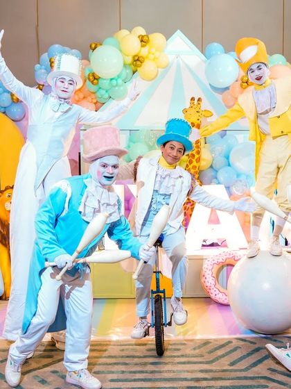 The birthday boy poses with a troupe of talented circus performers, including jugglers and a unicyclist, in front of the main stage.