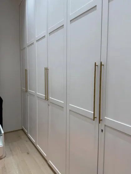 A shot of the floor-to-ceiling shaker-style wardrobe doors with elegant, long brass handles. This classic design provides massive amounts of storage while looking chic.