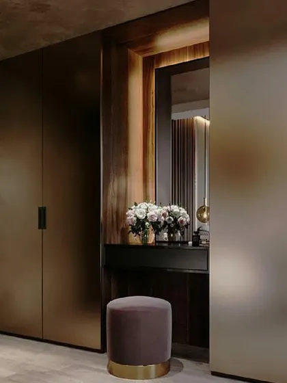 A sophisticated dressing area featuring floor-to-ceiling wardrobes with a smooth, matte bronze finish. The integrated vanity nook with a mirror and soft lighting creates a personal and luxurious corner.