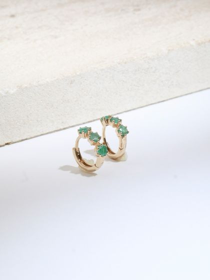 A close-up of the Petit Emerald huggie earrings, showing the tiny green emeralds that give them their charm.