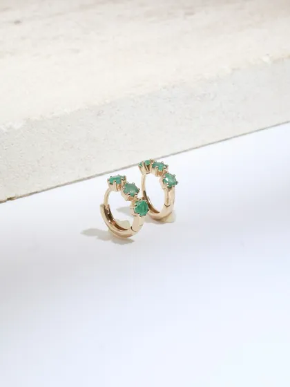 A close-up of the Petit Emerald huggie earrings, showing the tiny green emeralds that give them their charm.