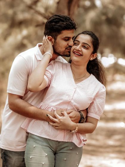 A tender moment during a pre-wedding shoot, with the groom kissing the bride's cheek as they walk through a sunlit path.