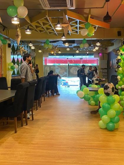 A football-themed party setup in a restaurant. The decor includes green and white balloon pillars topped with football balloons, perfect for a sports fan's birthday.