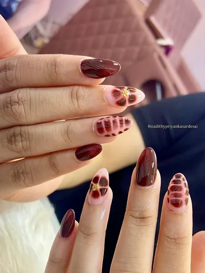 A close-up of the intricate burgundy nails, highlighting the glossy finish and the unique floral and plaid-like designs.