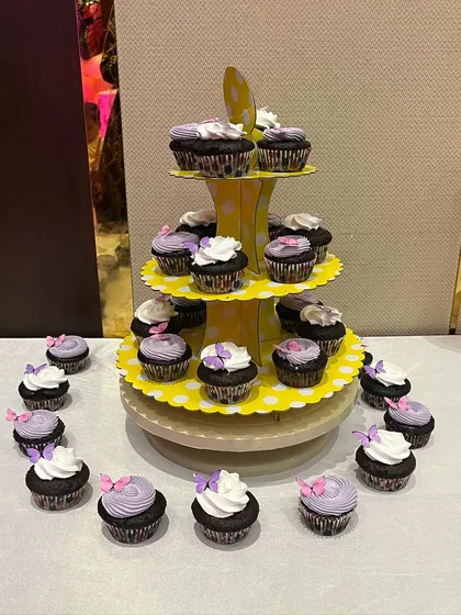 A tiered stand of beautiful butterfly cupcakes with purple and white frosting.