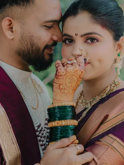 A detailed close-up focusing on the bride's henna-adorned hand, her traditional nath, and the loving gaze of her groom.