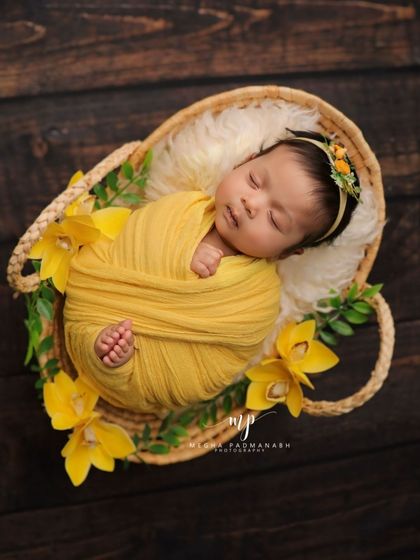 A classic overhead shot of a newborn sleeping peacefully in a basket. The yellow wrap and flowers create a bright and cheerful theme.