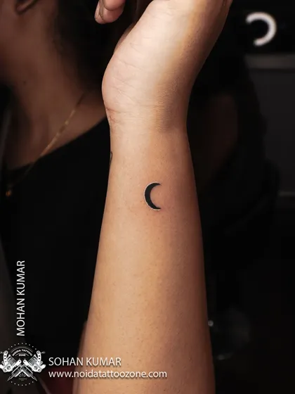 A tiny, solid black crescent moon tattoo on the wrist. This is a perfect example of a minimalist tattoo that is both simple and beautiful.