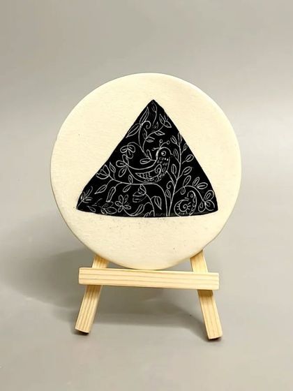 A circular tile with a sgraffito bird design inside a triangle. These small art pieces are a great way to elevate your interior design game.